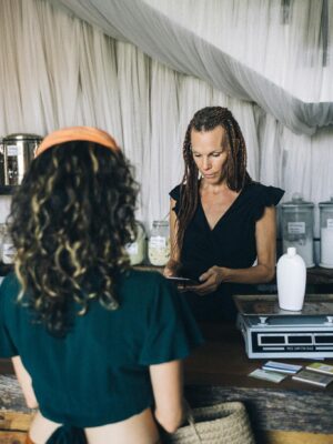 A woman completes a transaction at a boutique store's counter, interacting with a customer.