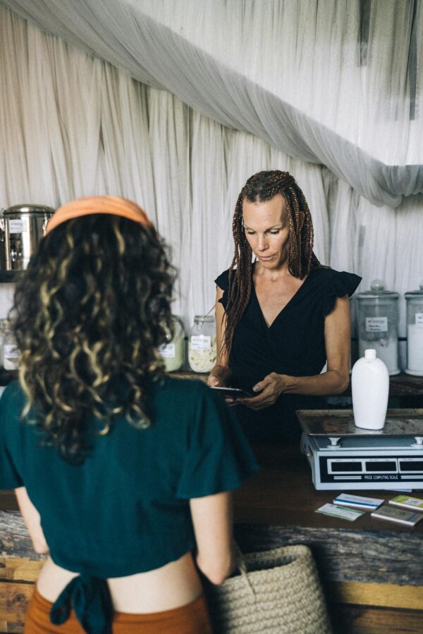A woman completes a transaction at a boutique store's counter, interacting with a customer.