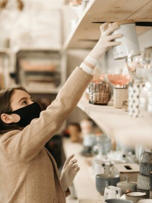 Woman wearing a mask and gloves shops in a boutique, practicing safety.